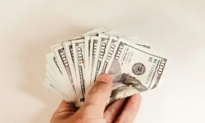 Dłoń trzymająca wachlarz banknotów 100-dolarowych.