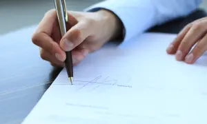 Dłoń podpisuje dokument piórem.