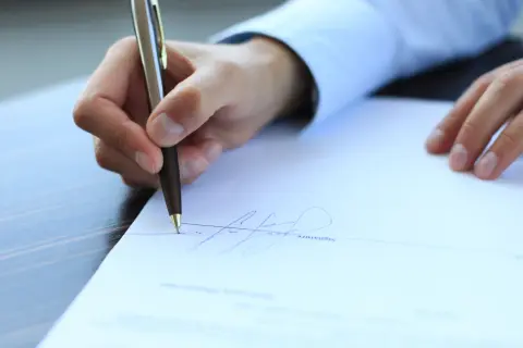 Dłoń podpisuje dokument piórem.