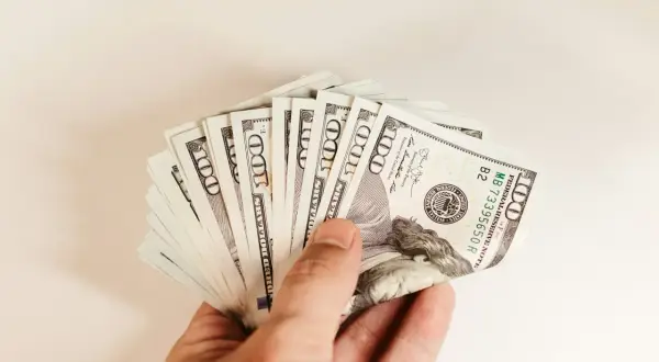 Dłoń trzymająca wachlarz banknotów 100-dolarowych.